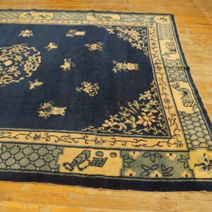 Navy rug with cream and sage floral patterns and a wide segmented border resting on distressed wood floorboards.