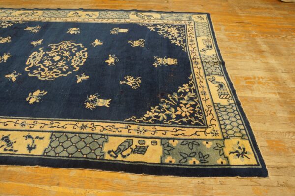 Navy rug with cream and sage floral patterns and a wide segmented border resting on distressed wood floorboards.