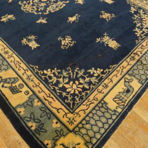 A navy blue rug with gold and sage intricate borders rests on distressed light wood flooring.