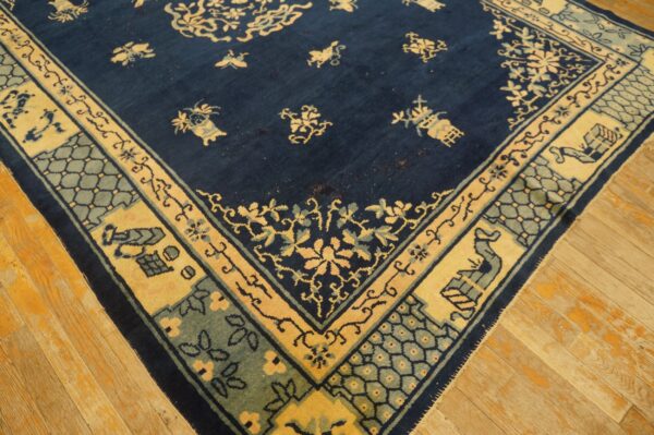 A navy blue rug with gold and sage intricate borders rests on distressed light wood flooring.