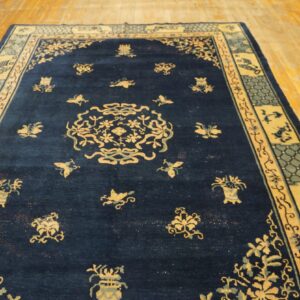Navy blue rug with a central medallion and detailed light-colored borders, displayed on a wooden floor.