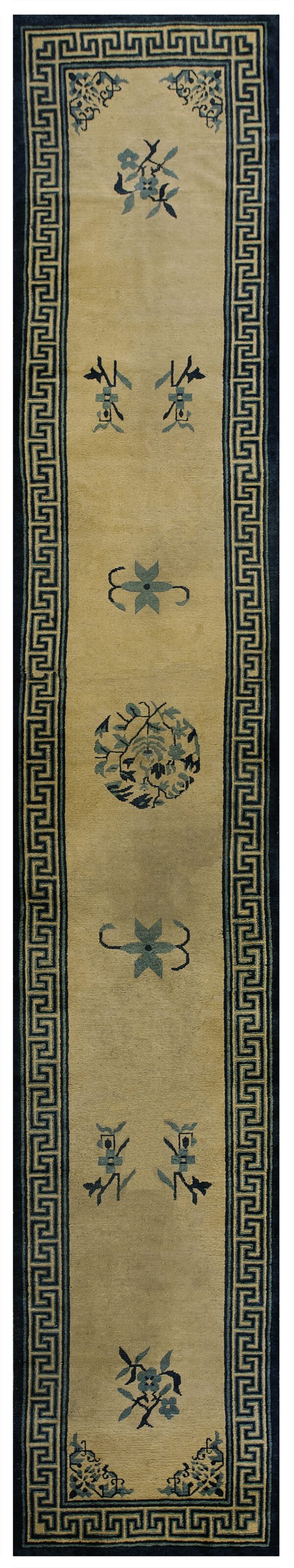 Long tan runner rug featuring scattered blue floral motifs and a greek key dark blue border.