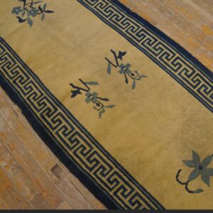 Gold runner rug with navy Greek key borders and stylized blue floral motifs lies on distressed wood planks.