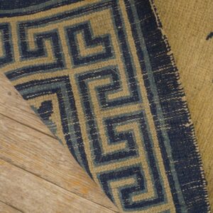 Tan rug with blue floral designs folds back, revealing a geometric blue border on wood flooring.