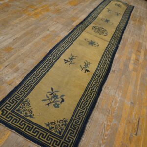 A gold runner rug with blue floral motifs and a Greek key border rests on distressed wood planks.