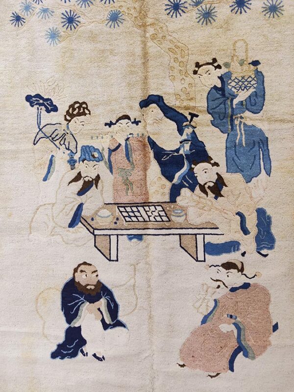 Cream pile rug featuring a figural scene of people gathered around a game table in blue and dusty pink.