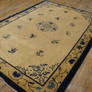 Cream rug with a wide gold and navy border and blue floral motifs rests on wood plank flooring.