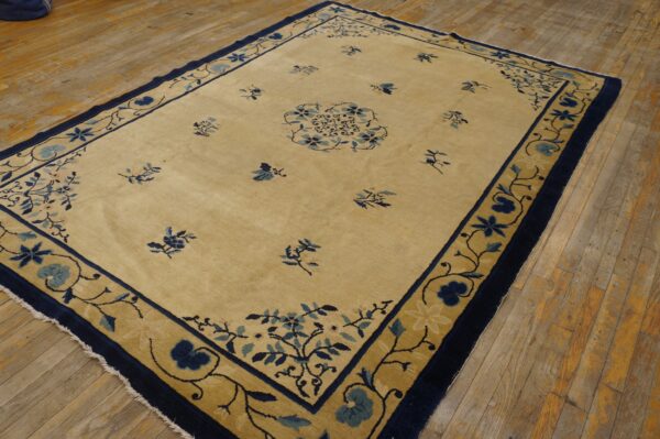 Cream rug with a wide gold and navy border and blue floral motifs rests on wood plank flooring.