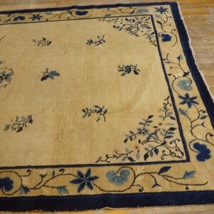 A pale yellow rug features scattered blue floral motifs and a wide navy blue patterned border on wood plank flooring.