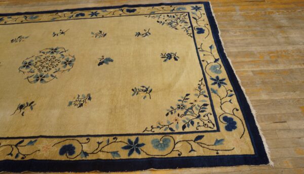 A pale yellow rug features scattered blue floral motifs and a wide navy blue patterned border on wood plank flooring.