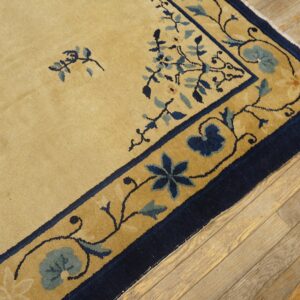 Close-up of a camel rug with scattered blue floral sprays and a navy blue border on rustic wood planks.