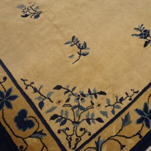 Short pile rug featuring a golden tan field and a navy blue vine and floral border over wood floorboards.