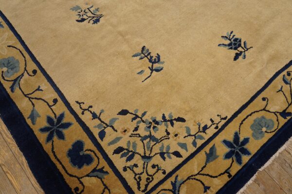 Short pile rug featuring a golden tan field and a navy blue vine and floral border over wood floorboards.