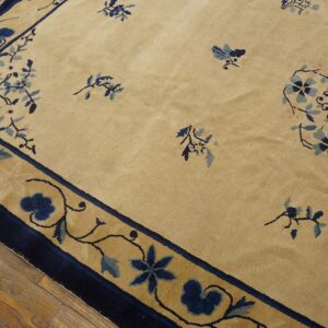 Tan rug with scattered dark blue floral sprays and a wide scrolling border on wooden floors.