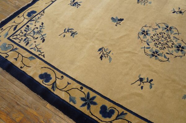 Tan rug with scattered dark blue floral sprays and a wide scrolling border on wooden floors.