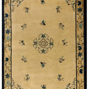 Tan rug with navy and teal floral border, a central medallion, and scattered motifs.