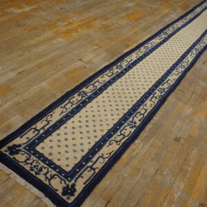 Navy blue and beige runner rug with geometric and floral borders lies on rustic hardwood flooring.
