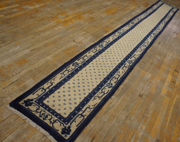 Navy blue and beige runner rug with geometric and floral borders lies on rustic hardwood flooring.