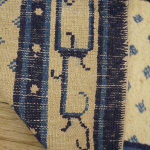 Beige and blue low-pile rug detail showing geometric motifs and vertical borders on wood floor.