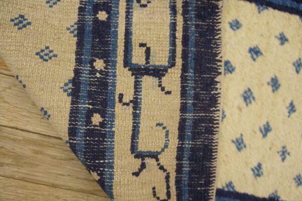 Beige and blue low-pile rug detail showing geometric motifs and vertical borders on wood floor.