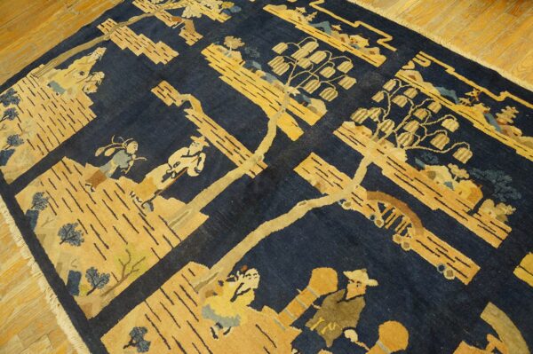 A navy blue rug with a golden yellow patterned landscape featuring stylized people and trees rests on wood flooring.
