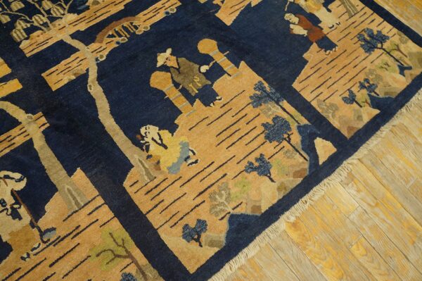 Navy blue and gold pictorial rug with stylized figures and trees rests on light wooden planks.