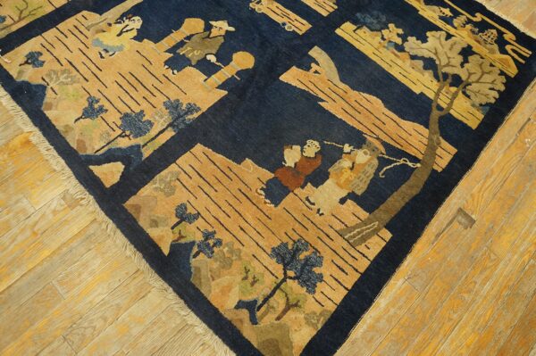 Navy blue and tan pictorial rug with human figures and trees displayed on worn light hardwood planks.