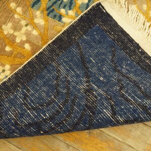 Flipped floral rug showing yellow, blue, and brown pile, dark blue backing, and white fringe on wood floors.