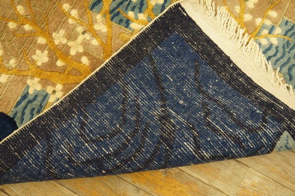 Flipped floral rug showing yellow, blue, and brown pile, dark blue backing, and white fringe on wood floors.