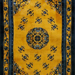 Gold rug featuring a complex navy blue medallion, scattered florals, and a key-patterned border.
