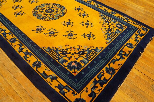 A vibrant yellow rug with dark blue patterns and teal accents rests on light brown wooden planks.
