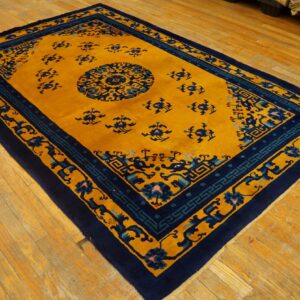 Rectangular rug with a golden field, central medallion, and navy blue geometric borders on wood flooring.