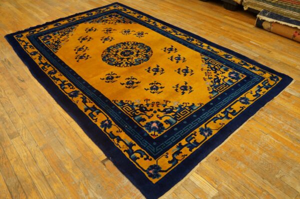 Rectangular rug with a golden field, central medallion, and navy blue geometric borders on wood flooring.