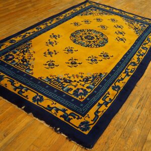 Gold rug featuring blue floral patterns and geometric borders rests on diagonal wooden plank flooring.