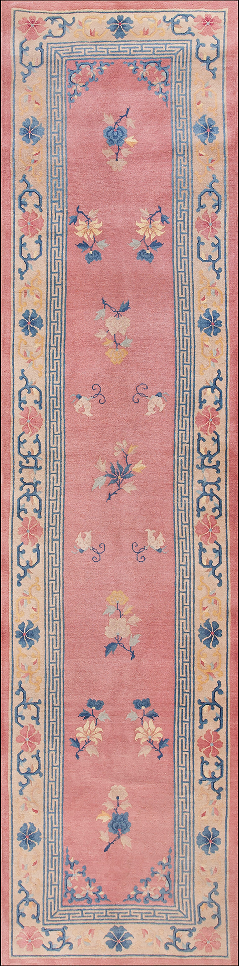 Pink runner rug with scattered blue and yellow blossoms and a wide cream border with blue geometric patterns.