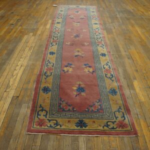 Pink runner rug with blue and yellow floral motifs and patterned borders on rustic wood floors.