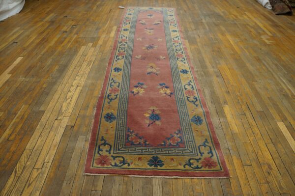 Pink runner rug with blue and yellow floral motifs and patterned borders on rustic wood floors.