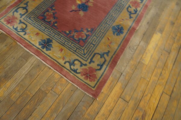 Low pile rug in dusty rose, gold, and blue floral motifs covers a distressed wood floor.