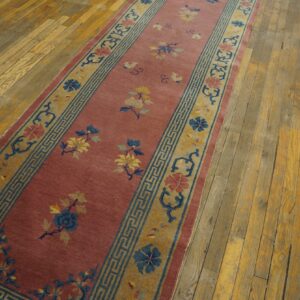 A long runner rug with a dusty rose field and blue and gold floral pattern sits on worn hardwood flooring.