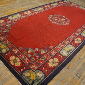 Red, low-pile rug with blue and beige floral borders and a central medallion on distressed wood floors.