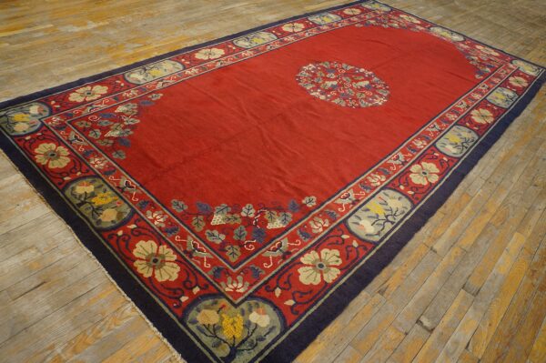 Red, low-pile rug with blue and beige floral borders and a central medallion on distressed wood floors.