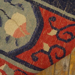 Geometric floral patterns in red, navy, yellow, and sage detail a low-pile rug over distressed wood.