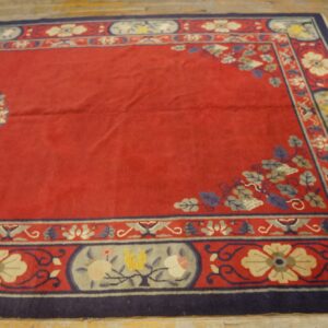 A red rug with a central medallion and complex floral border rests on light, distressed wood floors.