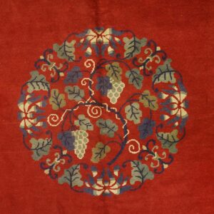 Red rug field with a central circular medallion of green and blue grapevines and fruit clusters.