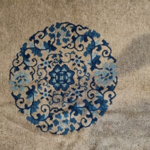 Detailed view of a tan high-pile rug showing a circular floral medallion design in dark and light blue.