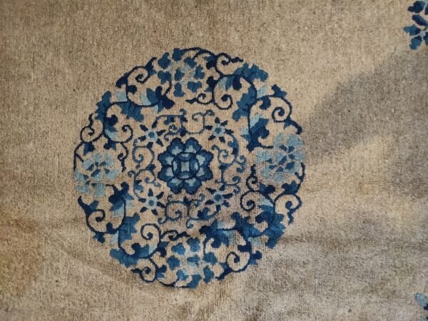 Detailed view of a tan high-pile rug showing a circular floral medallion design in dark and light blue.