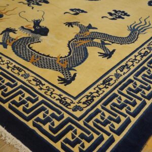 Navy blue dragon rug on a yellow field with geometric borders, lying on light brown wood flooring.