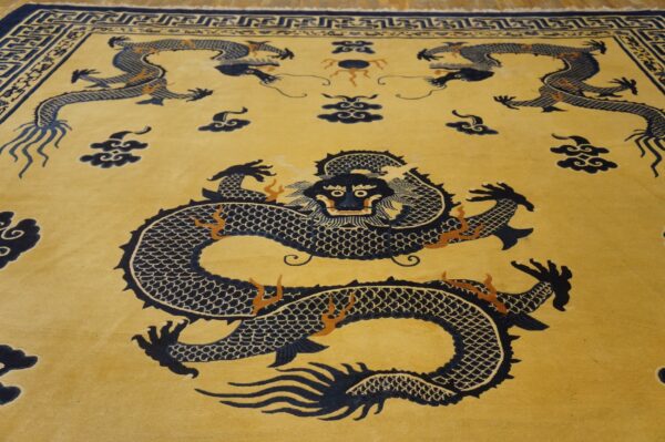 Gold rug featuring large navy blue dragons and clouds, surrounded by a complex geometric border.