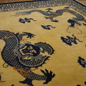 Golden yellow rug featuring large navy blue dragons and clouds, detailed with orange accents and a geometric border, resting on wood floor.