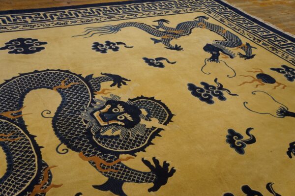 Golden yellow rug featuring large navy blue dragons and clouds, detailed with orange accents and a geometric border, resting on wood floor.